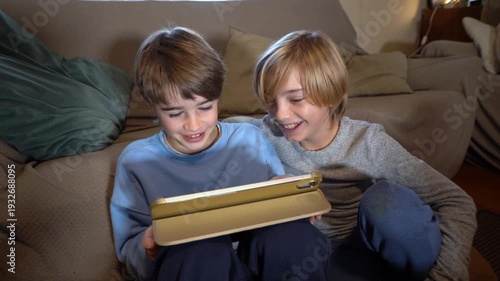 Two cheerful brothers laughing while watching a tablet
