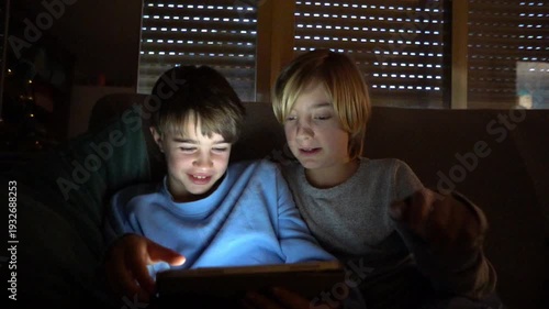 Two children playing on a tablet computer at night