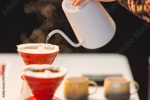 Photos Barista pouring boiling water from a white gooseneck kettle into a red ceramic V60 dripper