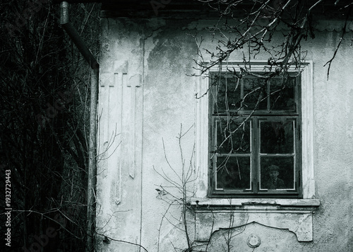 Chilling horror scene oif haunted house. Spooky little boy appears behind an old wooden window.