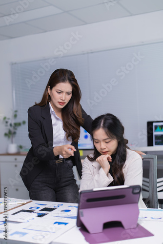 Billede på lærred Two Asian businesswomen in an office dispute over tablet reports; stern manager