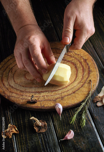 Obraz na plátne Hands are holding a knife while cutting a potato on a round wooden board