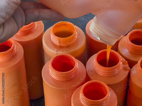 Focused close up of worker pouring orange liquid into plastic bottle. Industrial manufacturing process in factory, filling containers on production line with chemical paint