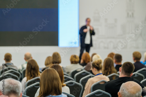 Rear view of attentive audience listening to presenter at business conference, professional networking, learning, corporate training atmosphere.