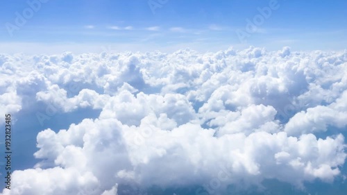 Aerial view from an airplane window flying over a sea of white, fluffy clouds in a blue sky