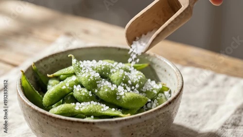 Salt falling on a bowl of edamame pods. Healthy green snack with plant protein. Cooking and healthy eating concept.