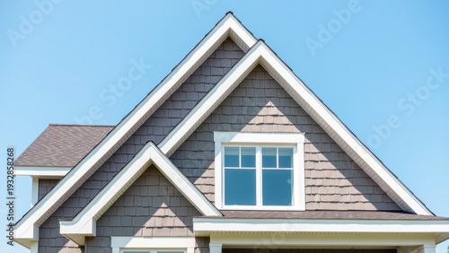 Modern house roof, gable architecture, gray shingle siding, white trim, residential home exterior, clear blue sky, bright and inviting