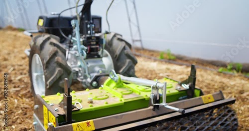 Farmer digging ground with power harrow farm tractor rotary tiller and and prepare the soil surface for seeding vegetable plants or turfing in the greenhouse