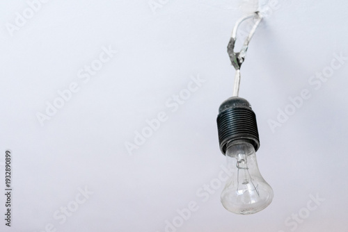 An incandescent lamp without a lampshade hangs from a white wall. The mounting bracket is clearly visible.