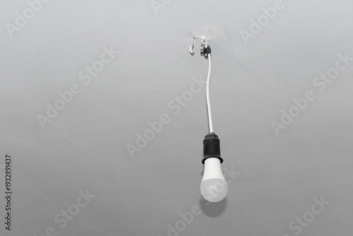 An LED lamp without a lampshade hangs on a white wall. The mounting bracket is clearly visible. Electric light bulb