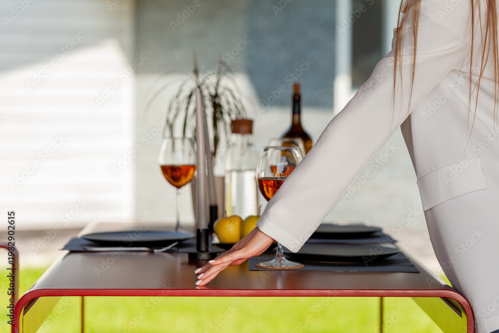 Fototapeta premium Woman in White Blazer Setting a Modern Red Outdoor Dining Table for a Garden Party