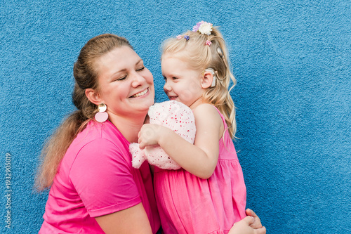 Deaf child with cochlear implant for hearing audio and aid for impairment having fun and laughs with mother outdoor in summer. Sound fitting device to help with communication listening and interaction