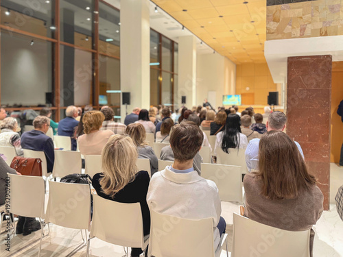 Conference audience sitting in conference hall during business seminar and presentation with speaker on stage and projection screen. Concept of conference networking, education and corporate training