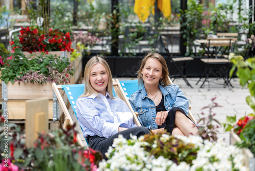 Portrait two young adult business woman girl friends relax sitting on deck chair in city park garden area point talk enjoy emotions smiling. Female persons leisure communication gossip talk outdoor