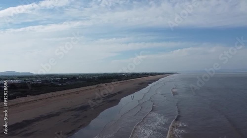 Forward flying drone tracking shot along Brean Sands beach heading towards the dramatic Brean Down headland on the UK coastline