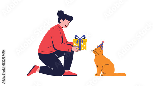 Young woman kneeling on the ground and offering a small yellow gift box to a cute ginger cat wearing a festive party hat.