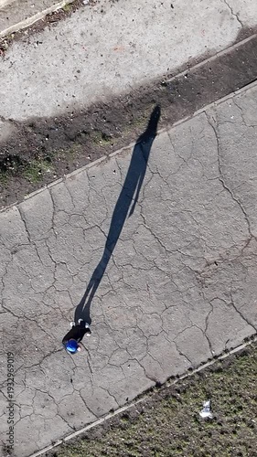 Athletic young man is walking along an asphalt road. Shadow from his body on a road. top view of the drone
