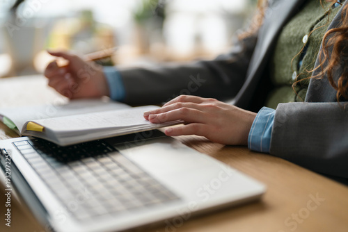 A person in professional attire reviews documents at a desk with a laptop, focusing on their work.