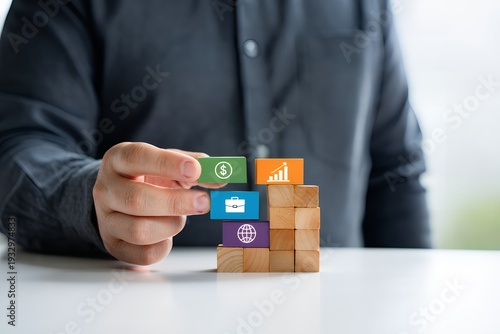 A man in a business shirt is building a structure with wooden blocks and colorful icons representing finance and growth