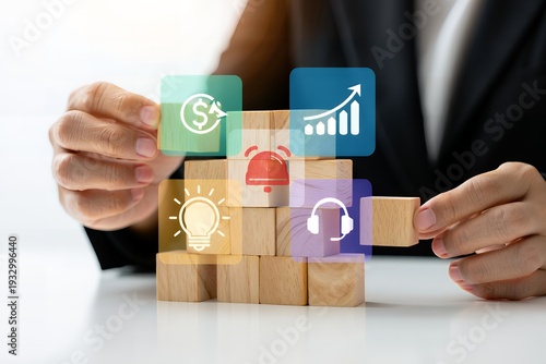 A person in a business suit is building a tower with wooden blocks with various business and communication icons floating above them.