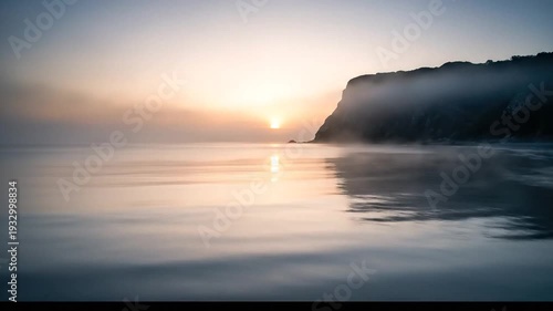 Misty Sunrise Over Calm Water With Coastal Cliff Reflection.