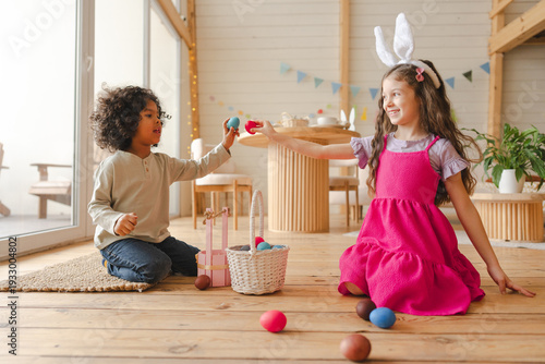 Happy diverse children playing with colorful Easter eggs on wooden floor
