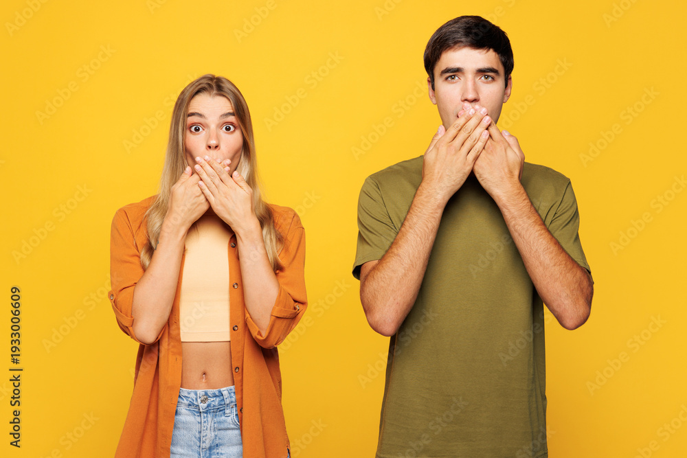 Fototapeta premium Young shocked sad surprised couple two friends family man woman wear casual clothes cover mouth with hand look camera together isolated on pastel plain light yellow color background studio portrait