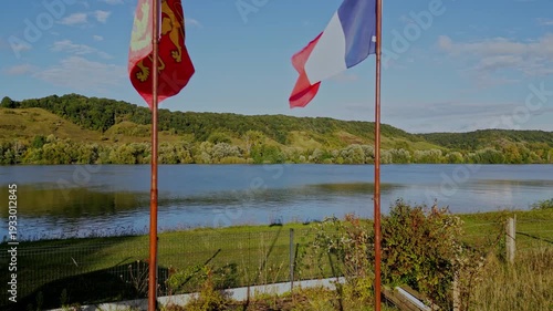 Drone footage flies between flags of Normandy and France to reveal beauty of rural countryside landscape scene with river Seine on sunny summer day at golden hour