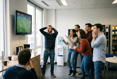 A group of young adult men and women in an office breakroom watching a live soccer match on a wall-mounted TV. They show intense emotional reactions, including shock, excitement, and disappointment.