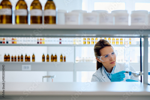 Fotografie Female scientist wearing protective eyewear and gloves carefully examining a gla