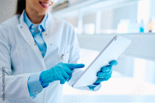 Female scientist wearing lab coat and blue gloves, interacting with a tablet computer during experimental data analysis in a modern facility