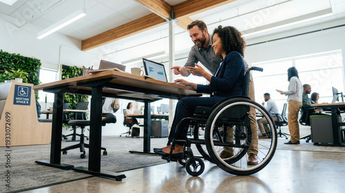 Businesswoman in wheelchair working on laptop with colleague.