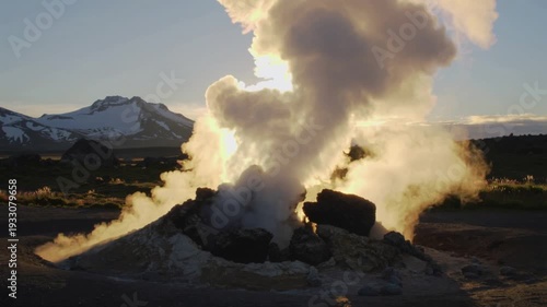Smoke billows from a geothermal vent in a mountainous landscape at sunrise