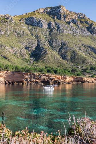 Vertical view of a white boat in turquoise Mediterranean waters under rugged mountains in Arta Mallorca
