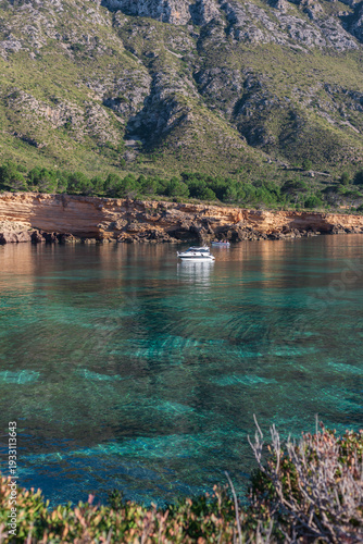 Stunning mountain backdrop over anchored boat in the clear waters of Playa Es Calo in Mallorca Spain