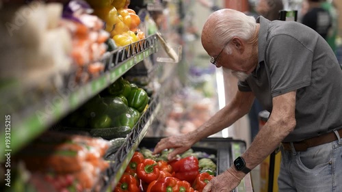 Senior man picks fresh vegetables at grocery store while shopping for food in the afternoon.