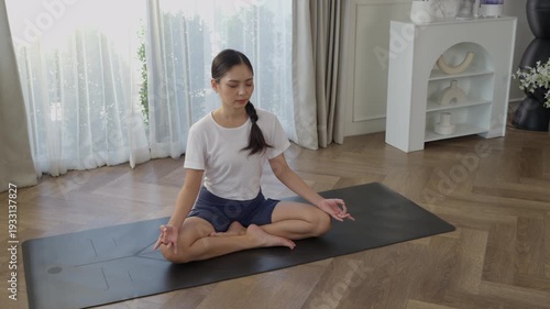 Asian woman yoga meditation lotus pose on mat at home, practicing breathing and concentration, wellness balance harmony for health