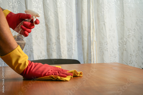 Person wearing red gloves cleaning table with spray and cloth