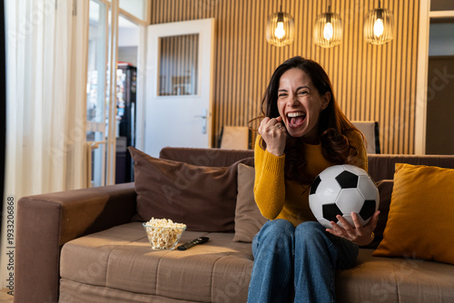 Excited woman celebrating goal while watching soccer on TV at home