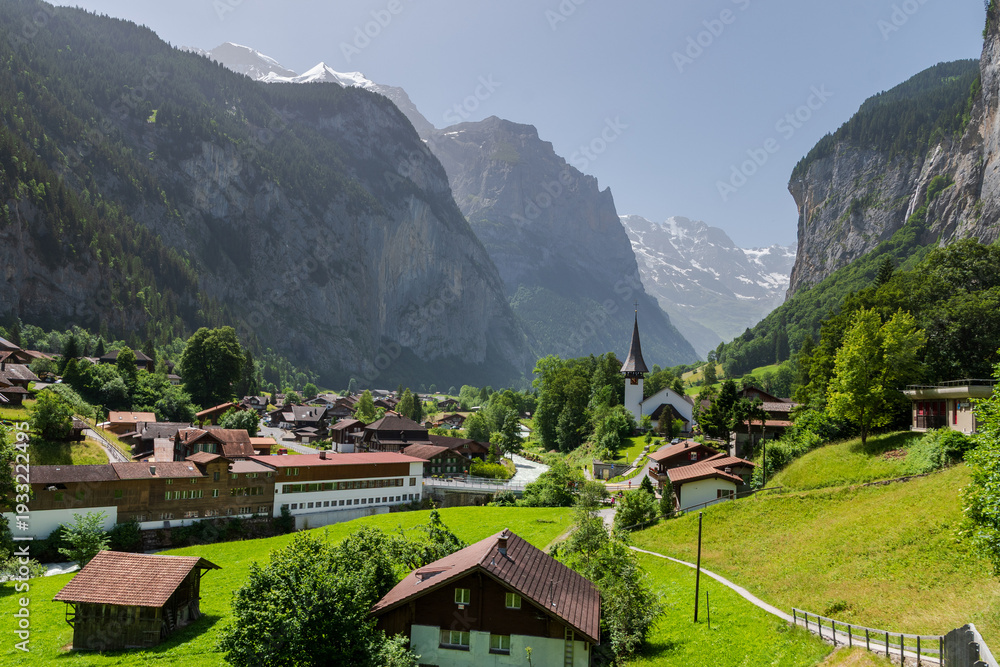 Obraz premium Scenic alpine village in Berner Oberland, Switzerland with church, green meadows, and dramatic mountains in summer