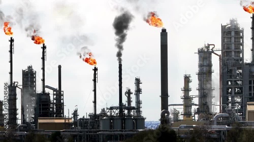 petrochemical oil refinery skyline with active gas flares and smoke plumes. 