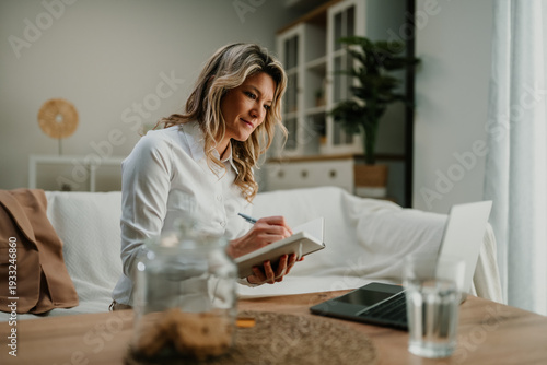 Wallpaper Mural Woman working remotely from home office, writing notes in notebook while using laptop on sofa Torontodigital.ca