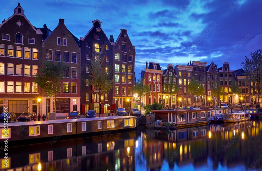 Obraz premium Amsterdam, Netherlands. Houses with nighttime illumination over canals with water in Old town. Quarter with traditional dutch houses. Night landscape. Blue hour.