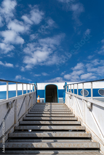 Steps lead up to an airplane waiting at the airport under a blue sky and clouds with no visible people around
