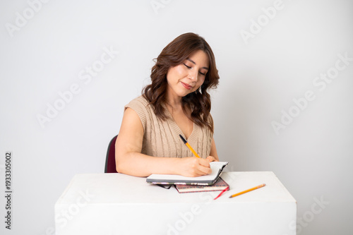 Mujer joven sonriente escribiendo en libreta en escritorio con fondo neutro