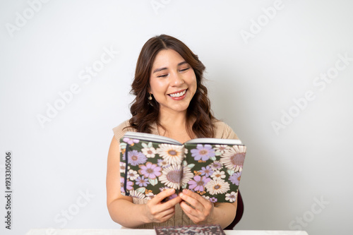 Mujer reflexiva leyendo libreta floral sobre fondo claro