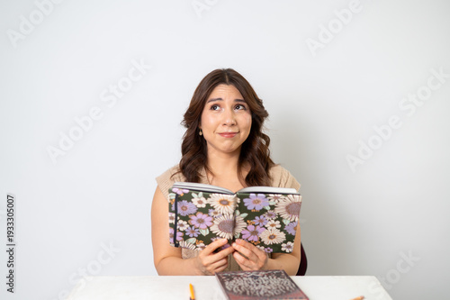 Mujer preocupada leyendo libreta floral sobre fondo claro