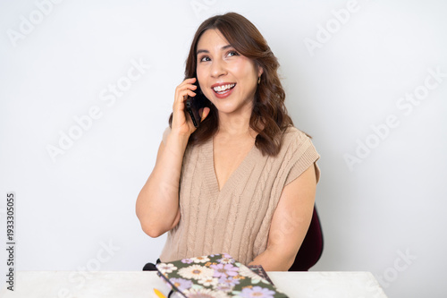 Mujer feliz hablando por teléfono móvil en escritorio con fondo claro