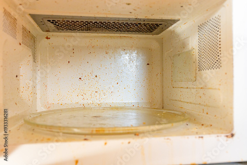 Dirty microwave interior full of food splatters and grime. Household appliance in need of cleaning. Unhygienic kitchen mess concept.