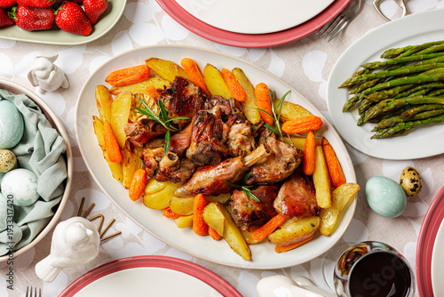 Homemade Easter dinner. Oval plate with Oven roasted Lamb with Carrots & Potatoes. Asparagus, colored easter eggs.  Strawberries, red wine. Festive table top view.